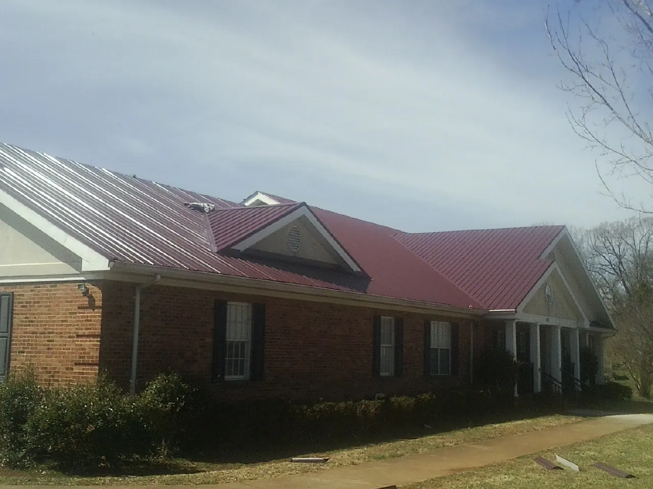 Red metal roof with gabled entries on a long brick building, from a Hail Damage Roof Repair job in Fenwick Island