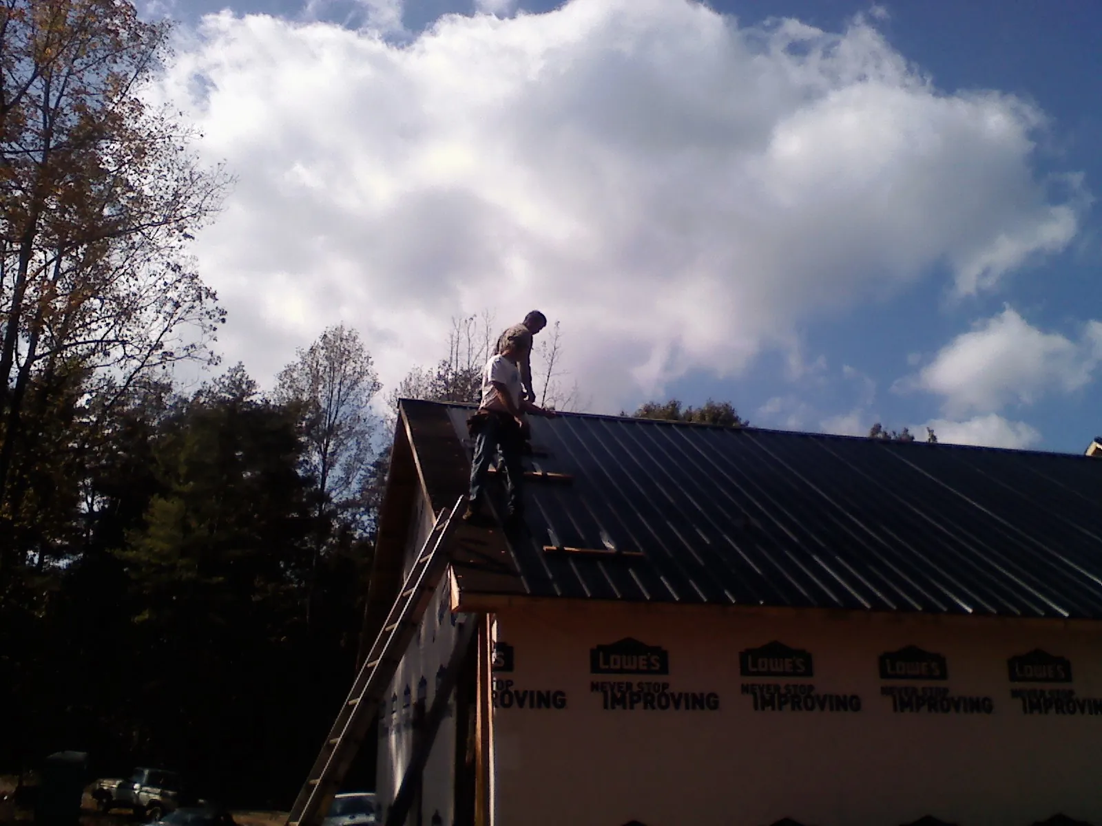 Roofer fastening dark metal panels high against a cloudy sky, from a Roof Inspection job in Fenwick Island