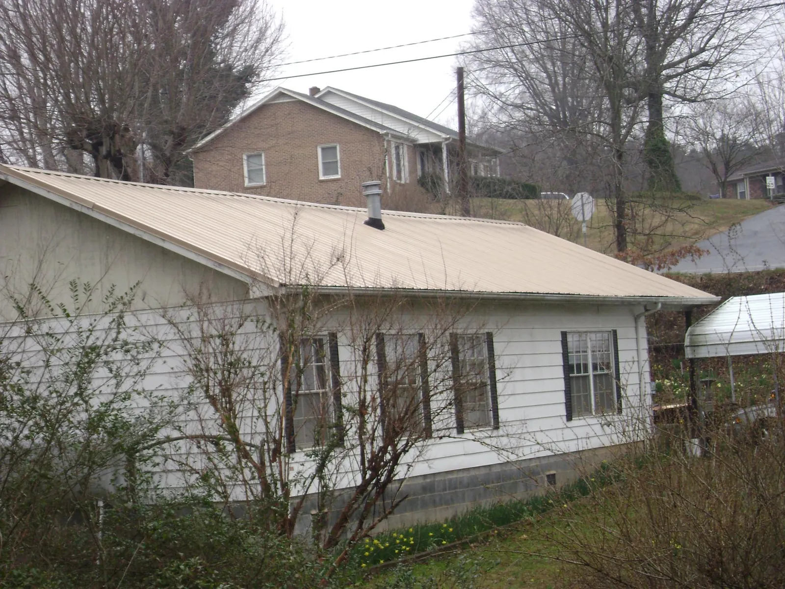 Tan metal roof on a white sided house set into a hillside — Commercial Roofing by Roofing Brothers in Fenwick Island